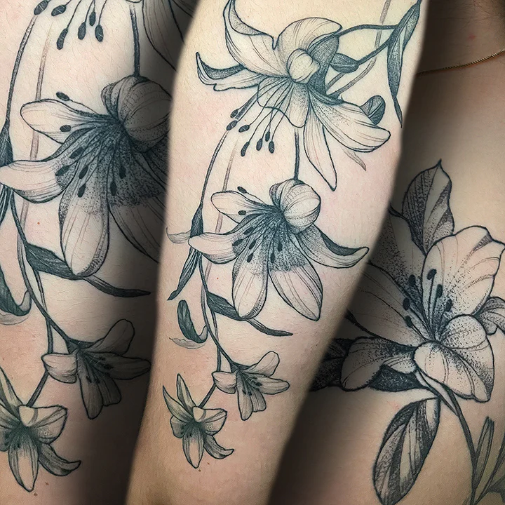 A sophisticated fine-line floral tattoo of lilies, featuring intricate stippled shading and clean, organic linework that flows with the natural shape of the arm.