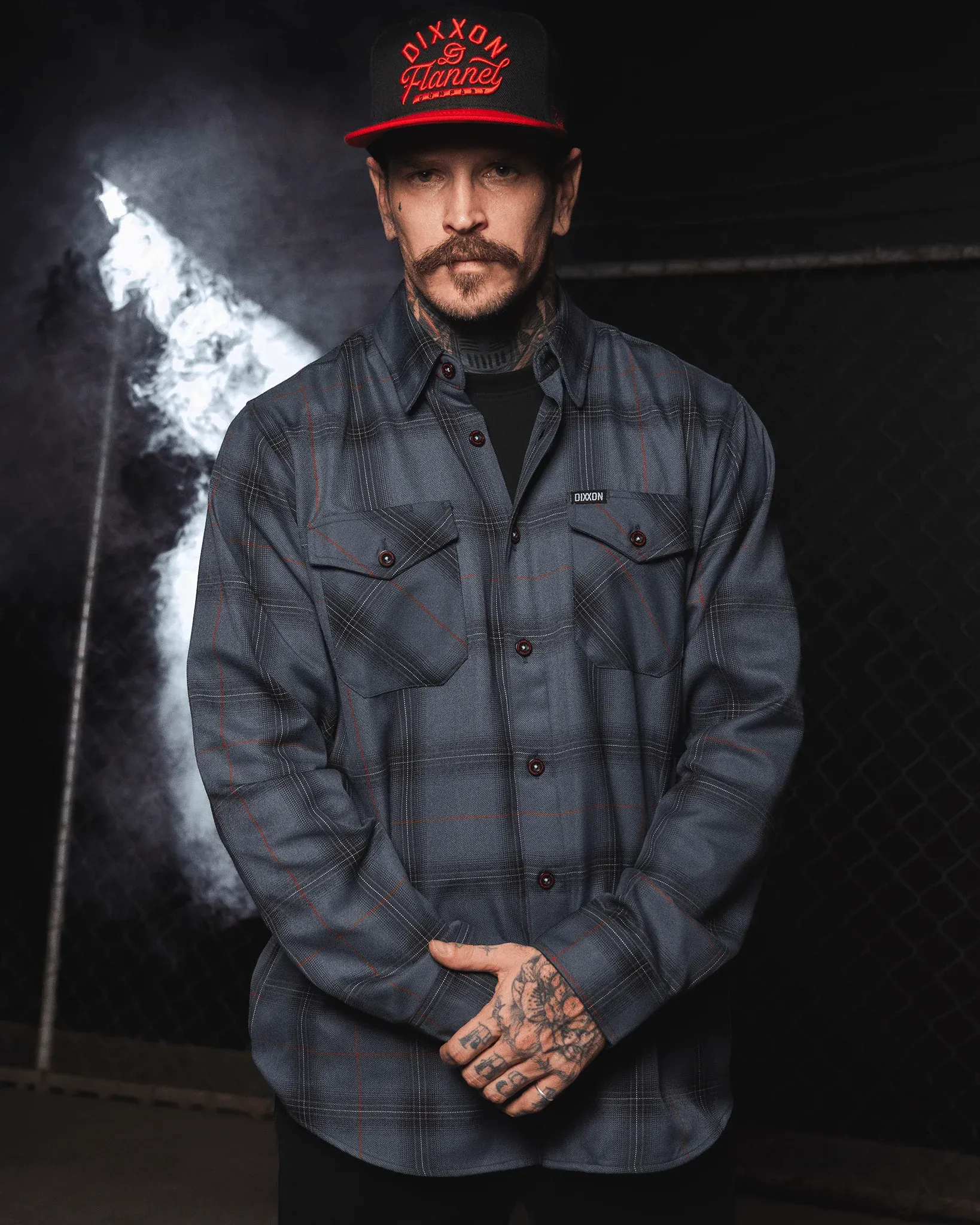 Man wearing dark gray and red grid Stealth flannel with tattooed hands and Dixxon hat.