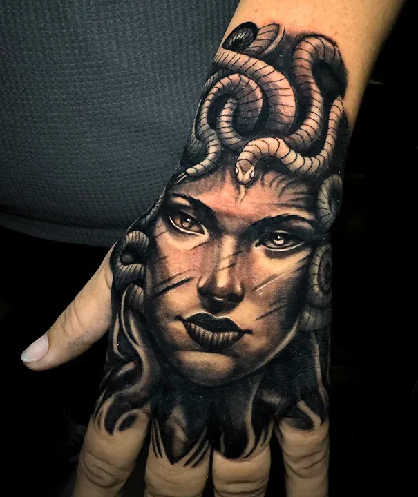 Black and gray realism hand tattoo featuring a detailed Medusa face with snake hair.
