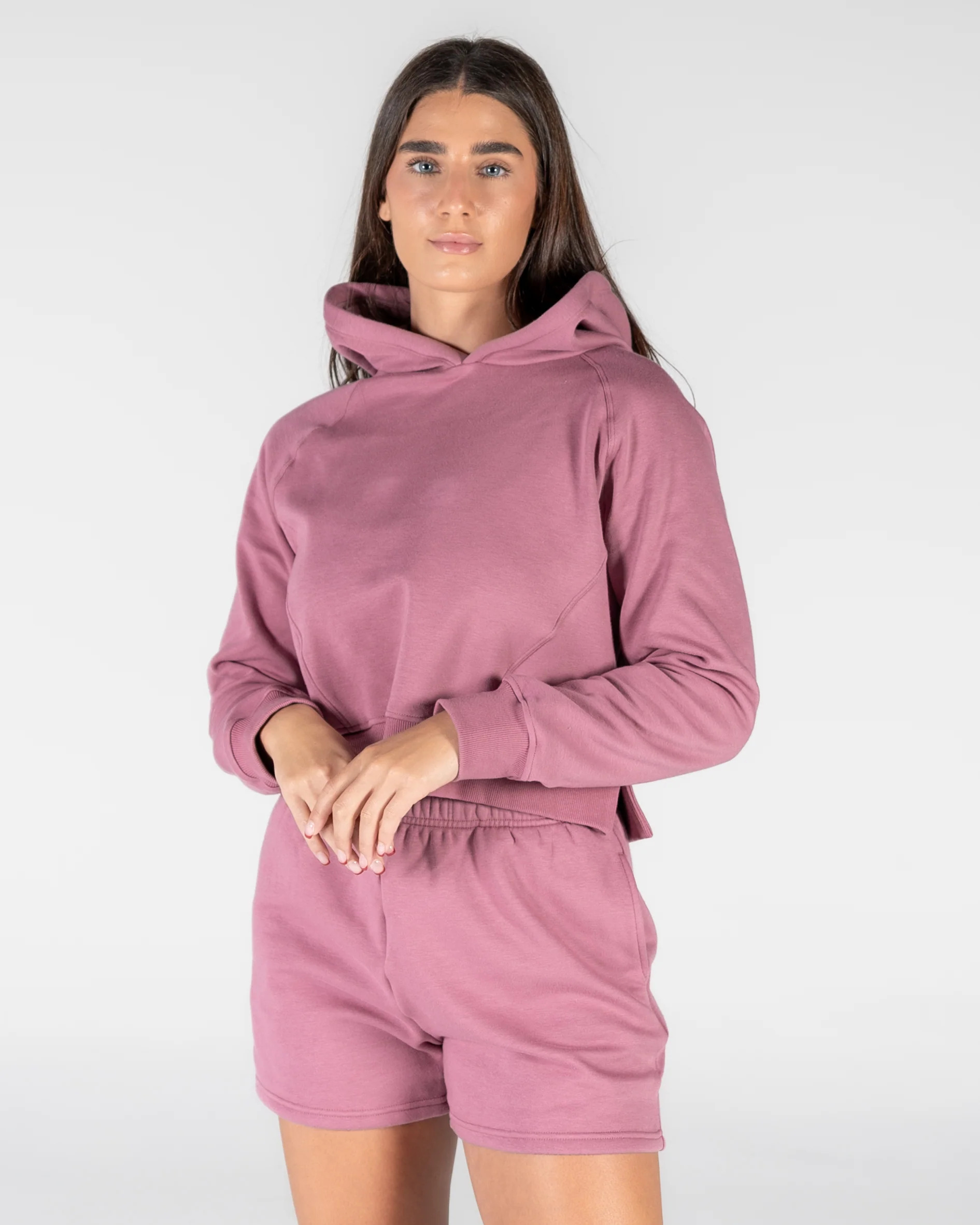 Studio portrait of a woman wearing a matching dusty rose athleisure set, featuring a structured cropped hoodie with long sleeves and coordinating lounge shorts.