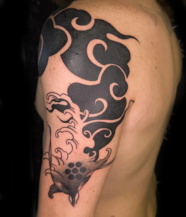 A large, bold Japanese-inspired tattoo covering a shoulder and upper arm, featuring heavy solid black wind bars and stylized crashing waves with an ornamental dot emblem at the base.