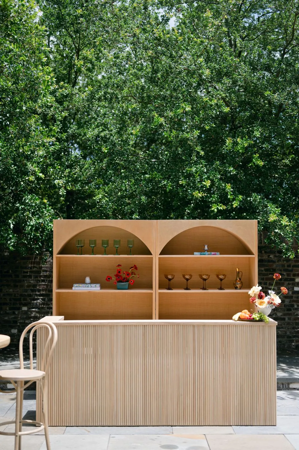 Luxury outdoor bar rental with arched shelving, ribbed front panel, glassware, flowers, and fruit display.