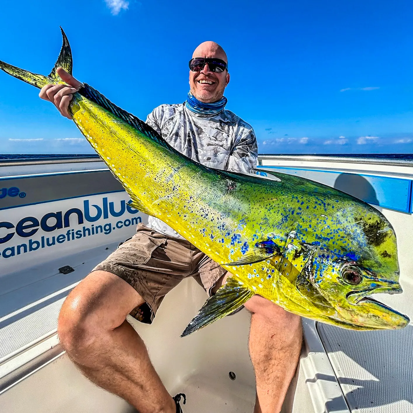 Angler holding a large mahi mahi (dolphinfish) on an Ocean Blue Fishing Adventures boat in Vanuatu, with the ocean and blue sky in the background.