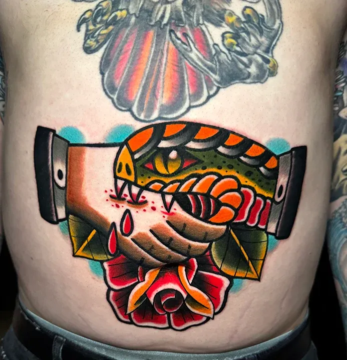 American traditional stomach tattoo of a snake biting a hand above a red rose.