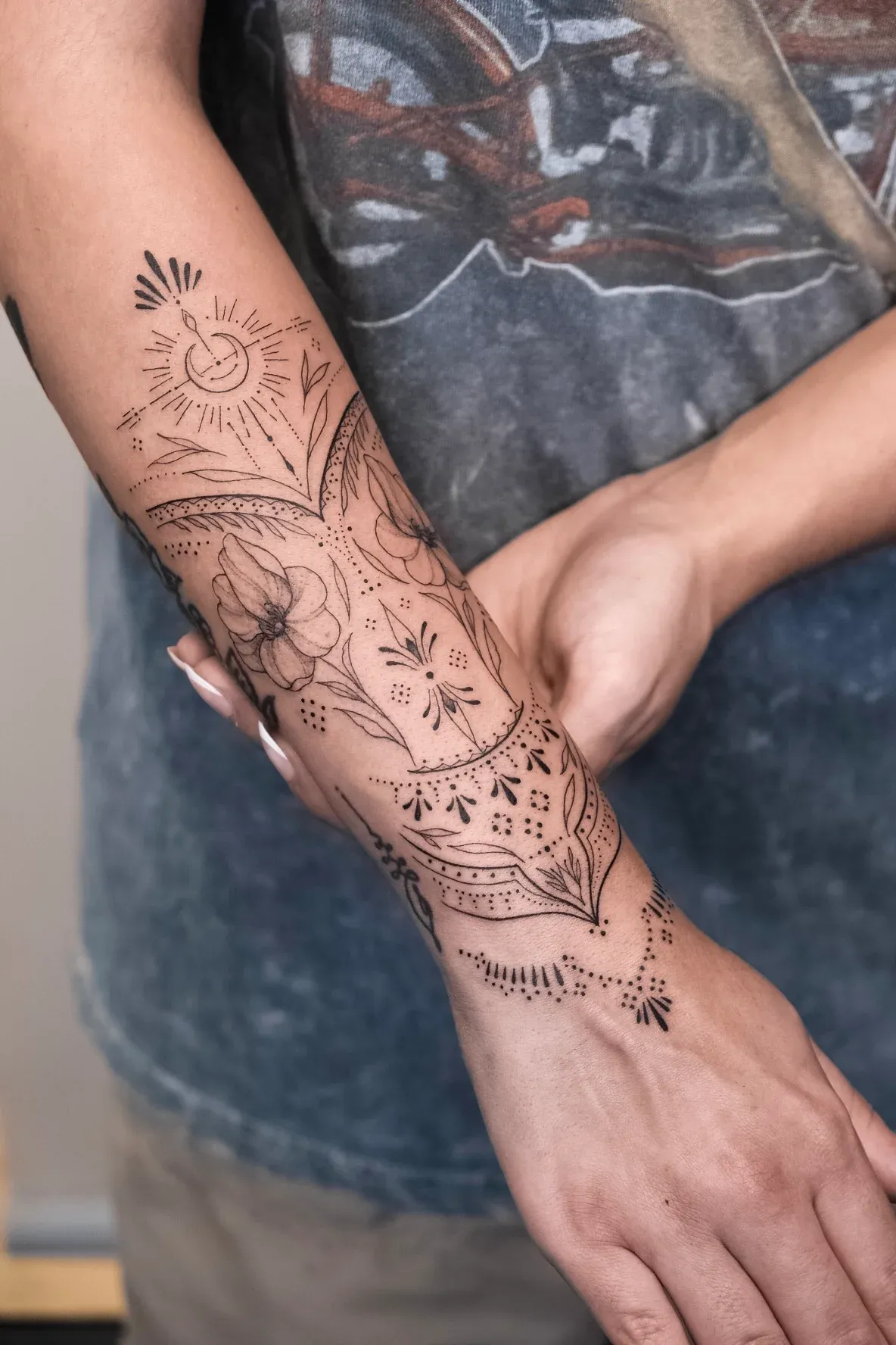Intricate fine-line ornamental forearm tattoo with floral elements, a crescent moon, and dotwork.