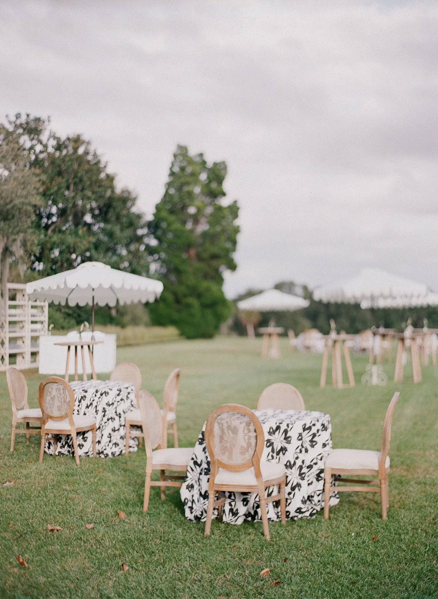 Garden birthday party setup with cocktail tables, black-and-white floral linens, bistro chairs, and white umbrellas.