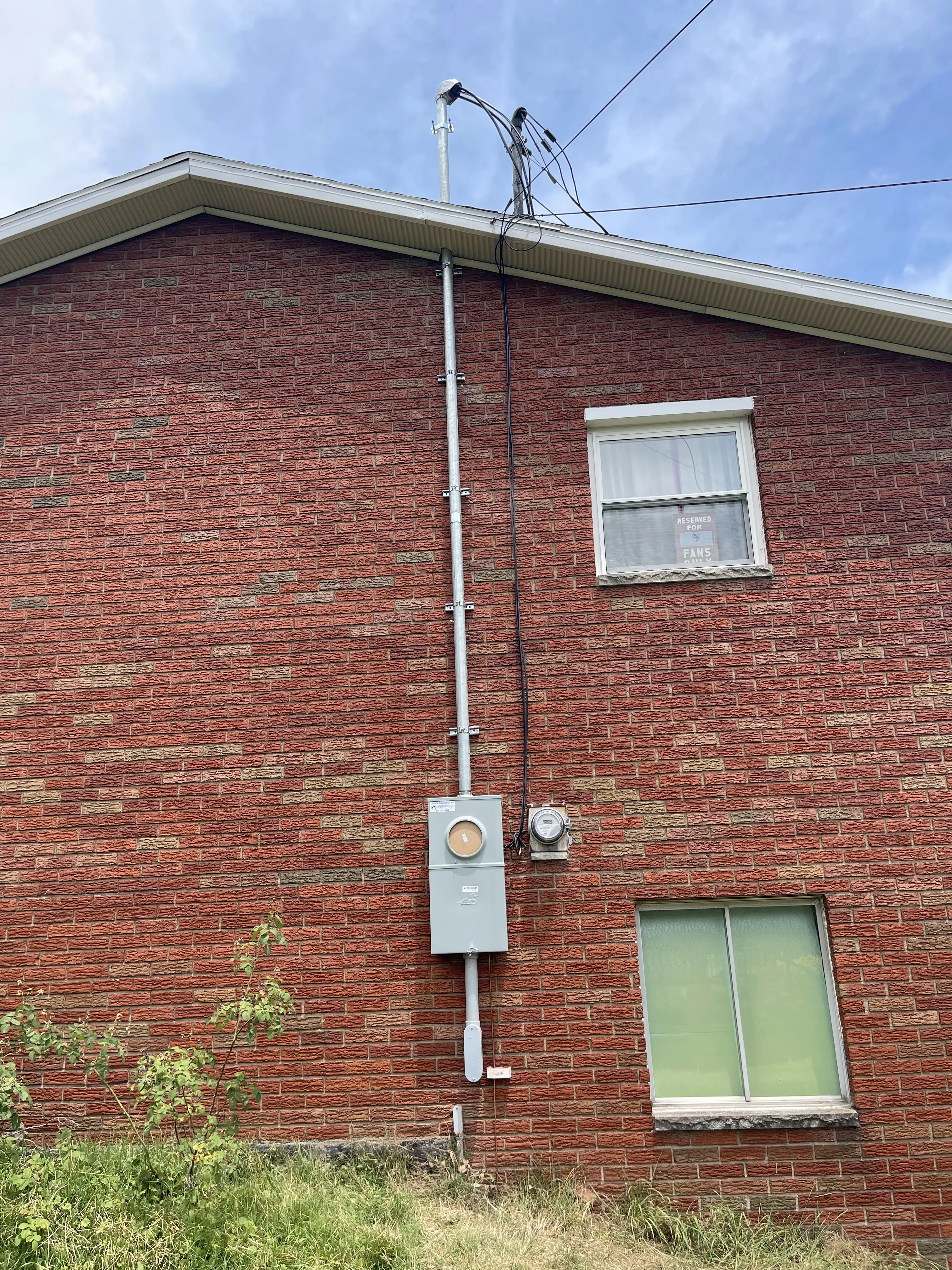 Residential house exterior showing electrical meter and main service panel on brick wall