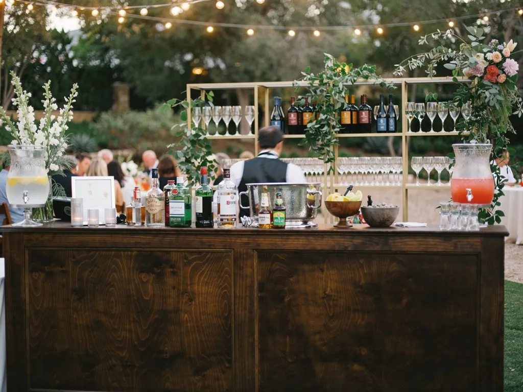 Behind-the-bar wedding setup with organized glassware shelving, champagne flutes, ice buckets, and bartender supplies