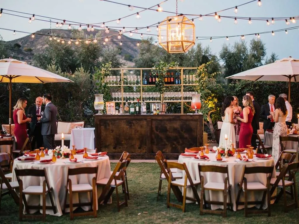 Full outdoor wedding beverage zone with crystal glassware, high-top tables, and floral accents in ambient