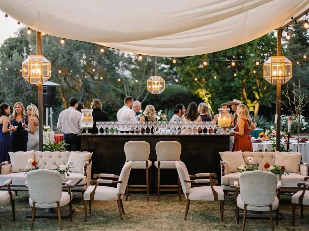 Outdoor wedding bar area with canopy shade, lounge seating, and glassware in a warm evening