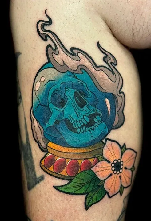 Colorful neo-traditional tattoo of a skull inside a crystal ball with smoke and a pink flower.