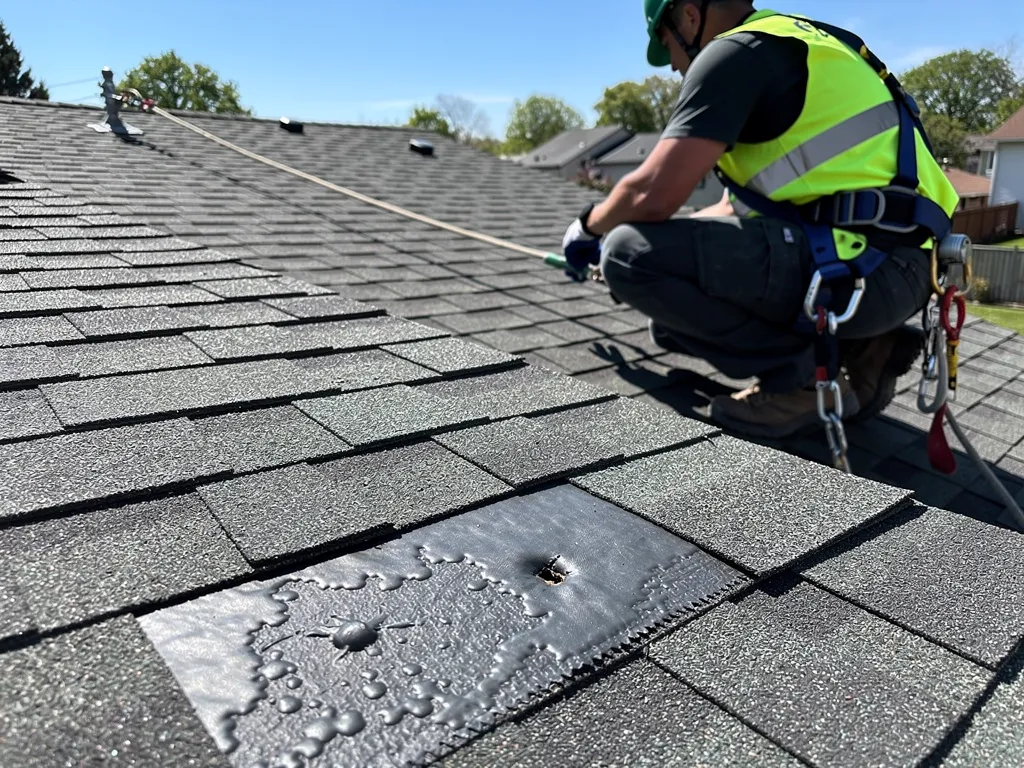 Roofer in helmet and harness examining blisters and punctures on a residential roof