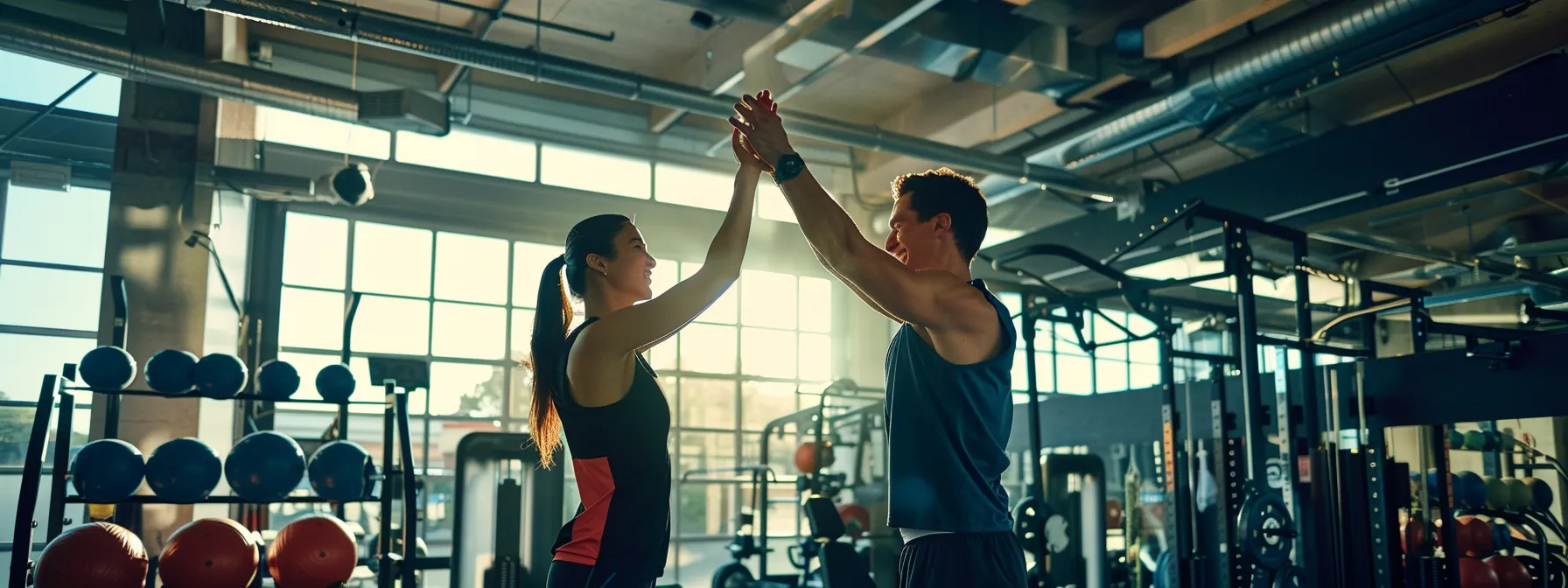 two individuals in workout gear high-fiving each other in a gym filled with fitness equipment.