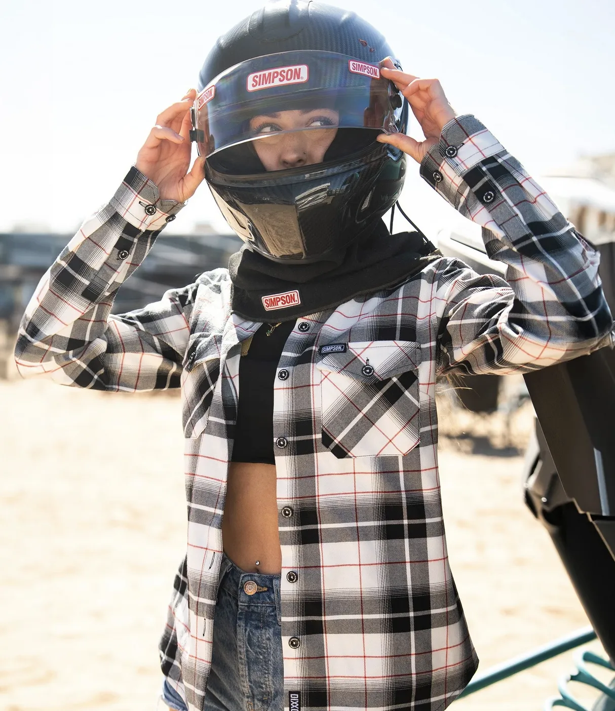 Young woman in desert setting looking at the camera and placing a motorcycle helmet away from her head, wearing Dixxon Women's Simpson Flannel