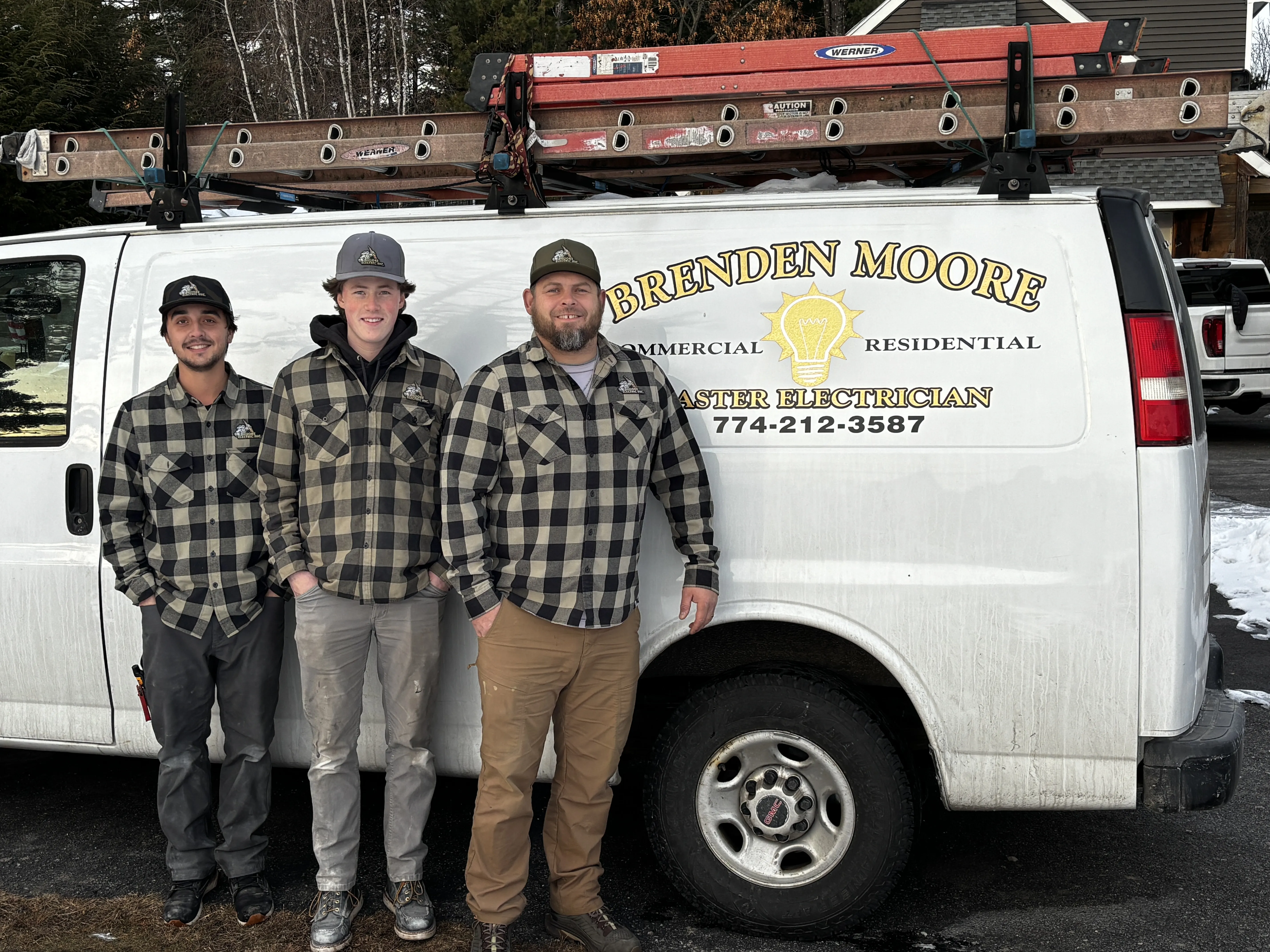 Three electricians in matching plaid shirts standing in front of a van with "Brenden Moore Master Electrician" branding, showcasing their expertise in residential and commercial electrical services.
