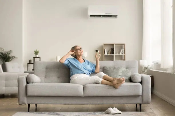 Homeowner relaxing in a cool living room with a wall-mounted AC unit, representing the value of transparent pricing in emergency AC repairs.