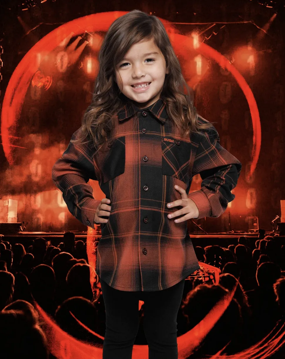 A young girl in a red and black Dixxon "BUSH" collaboration flannel poses confidently in front of a high-energy concert stage backdrop.