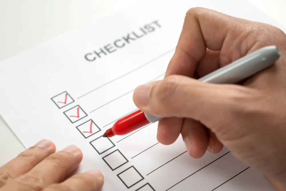 A person's hand is holding a red marker, checking a box on a paper labeled "CHECKLIST," with three preceding boxes already marked, possibly showing a step completed for a Roof Repair project.