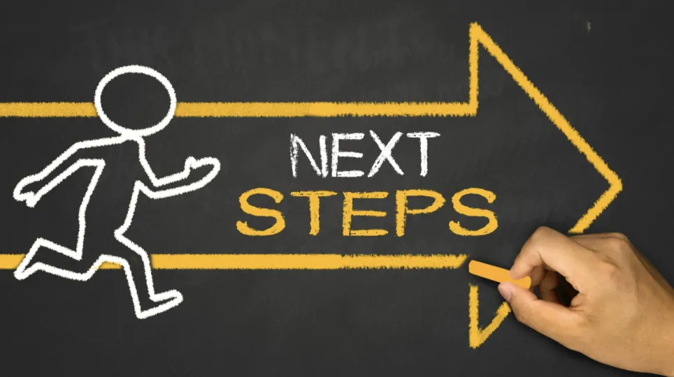 hand drawing an orange arrow with the words ‘next steps’ on a balckboard