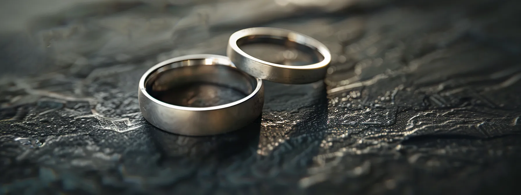 a close-up shot of two plain silver wedding bands side by side on a dark, smooth surface.