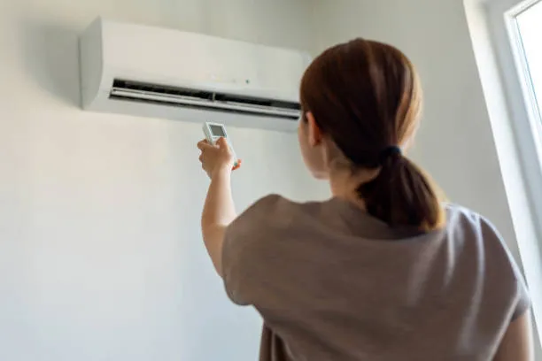 Homeowner using a remote to operate an AC unit, highlighting fast and reliable emergency AC repair services.