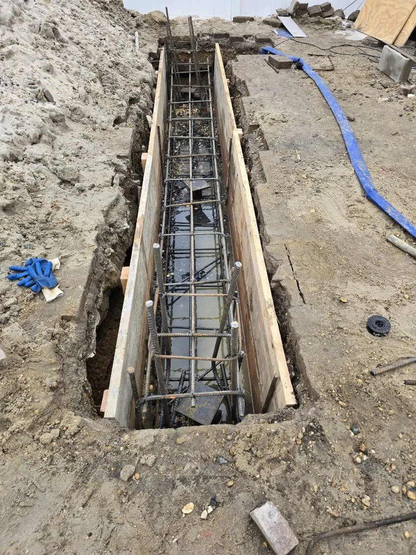 Preparation of a reinforced concrete grade beam. We use heavy-duty rebar cages to ensure the new foundation transition is structurally superior to the original.