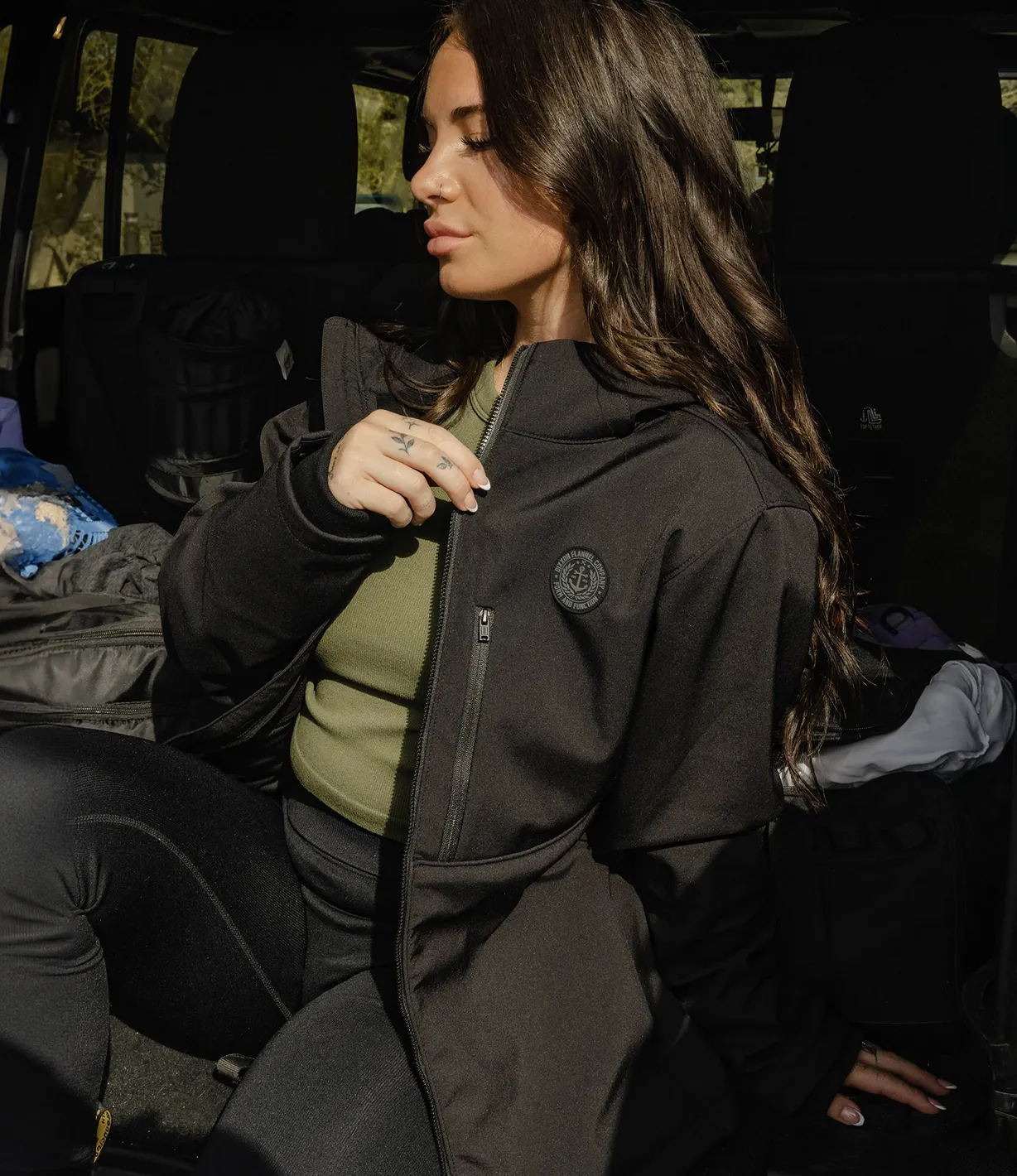 Woman sitting in open trunk of car showing logo of black Anchor Jacket