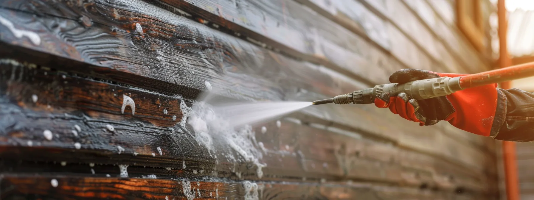 a person pressure washing the siding of a house, inspecting for damage and wear.