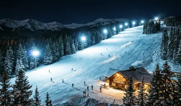 AI-generated image of illuminated night-skiing slopes with skiers under bright lights and a lodge in the distance. AI-generated image of illuminated night-skiing slopes with skiers under bright lights and a lodge in the distance.
