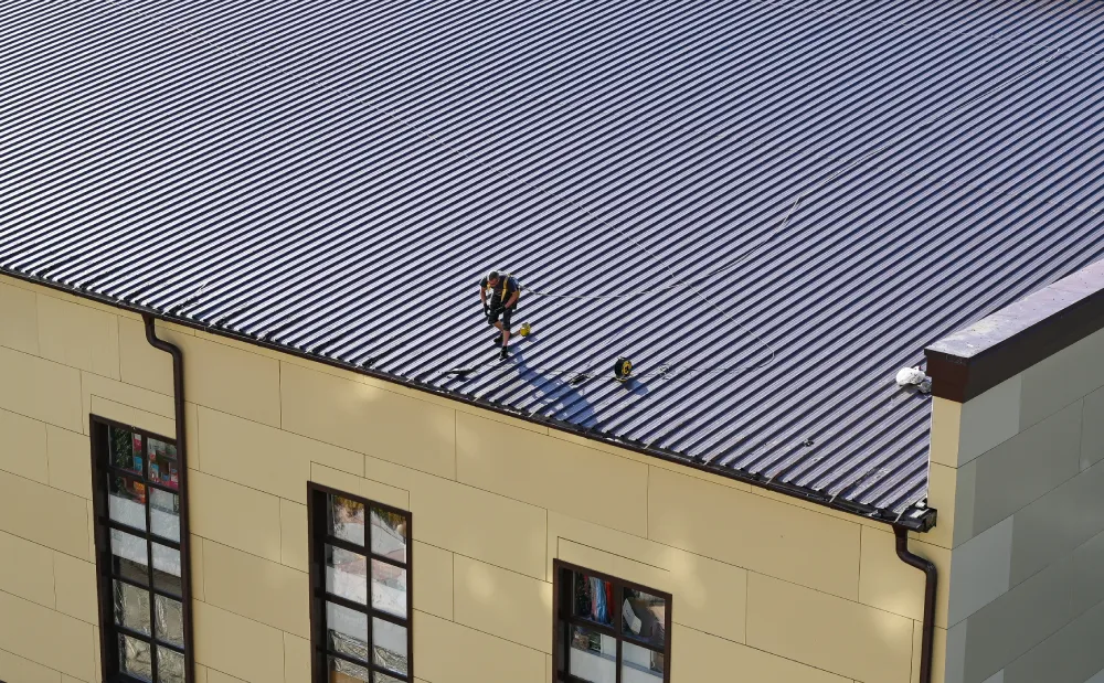 Aerial view of a professional contractor performing maintenance on a large, corrugated metal commercial roofing system on a multi-story building.