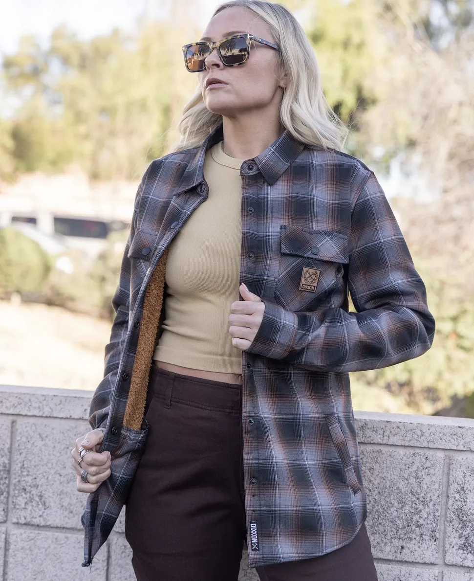A woman wearing sunglasses and a dark brown and gray plaid flannel jacket with a brown faux-sherpa lining and a leather-style Dixxon brand patch on the chest pocket.