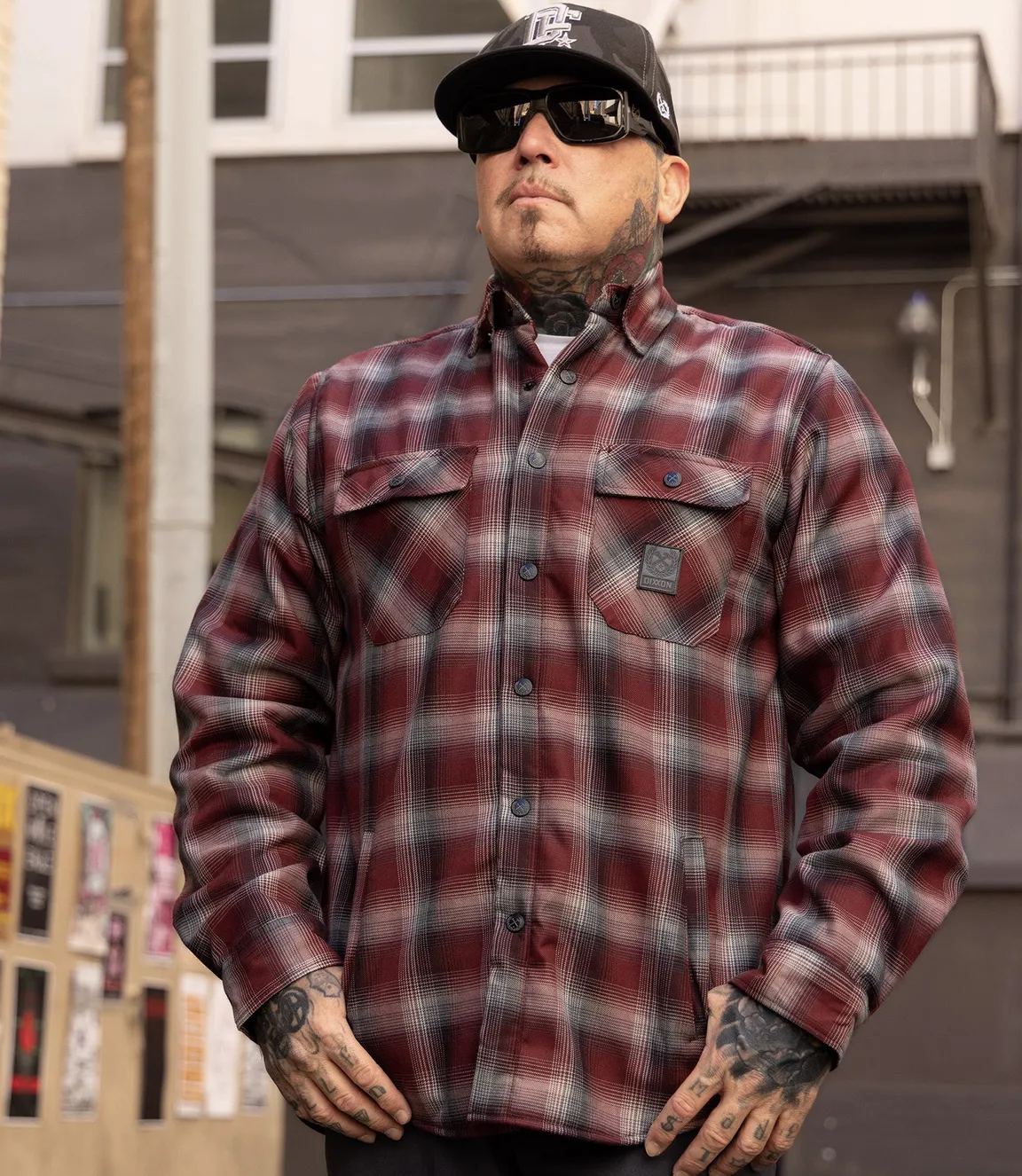 A person wearing a red and gray plaid Sherpa Lined Flannel Jacket with a black brand tag on the left chest pocket and dual front slash hand pockets.