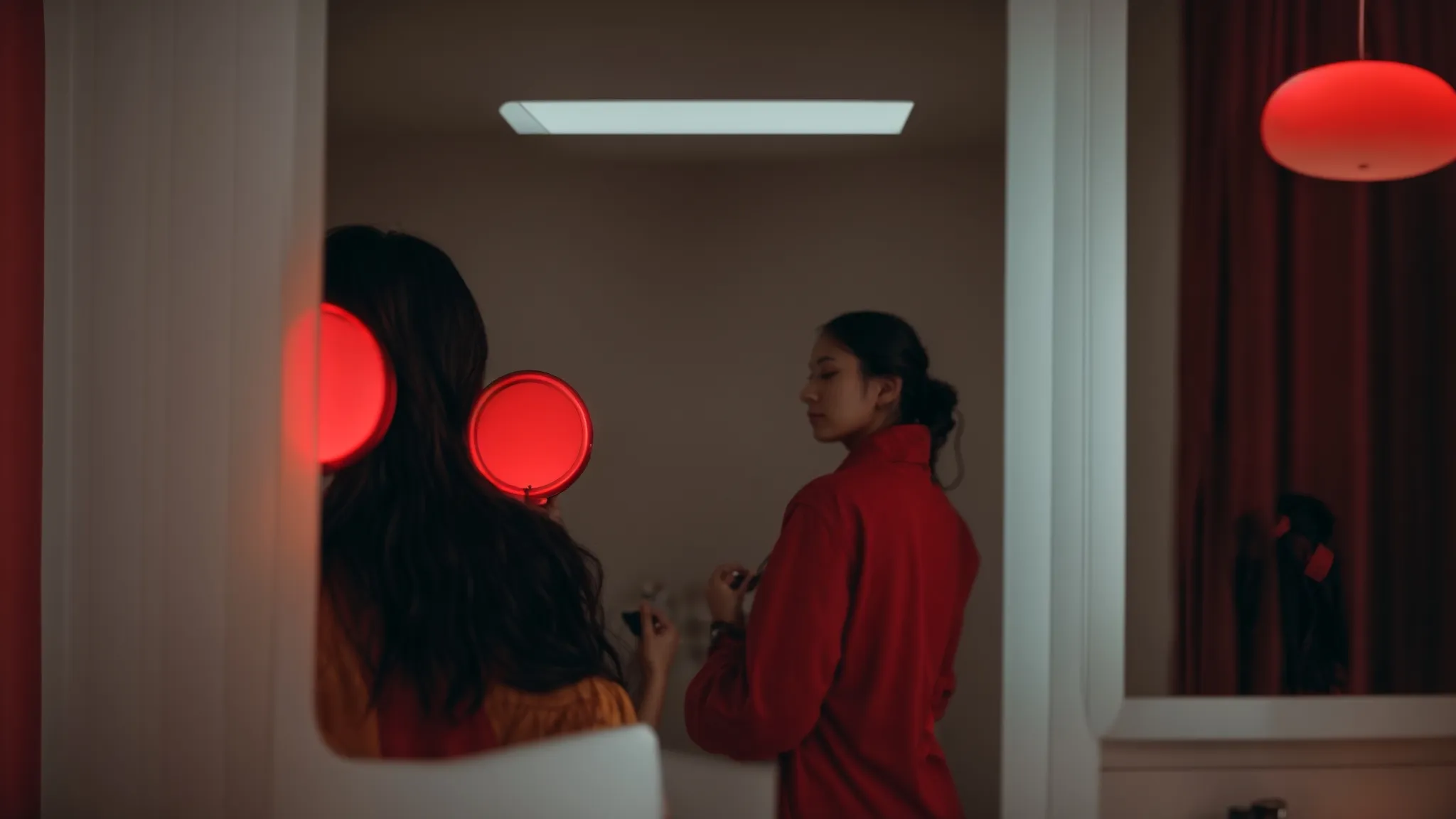 a person stands in front of a mirror, holding a red light therapy device close to their face, bathed in a soothing glow.