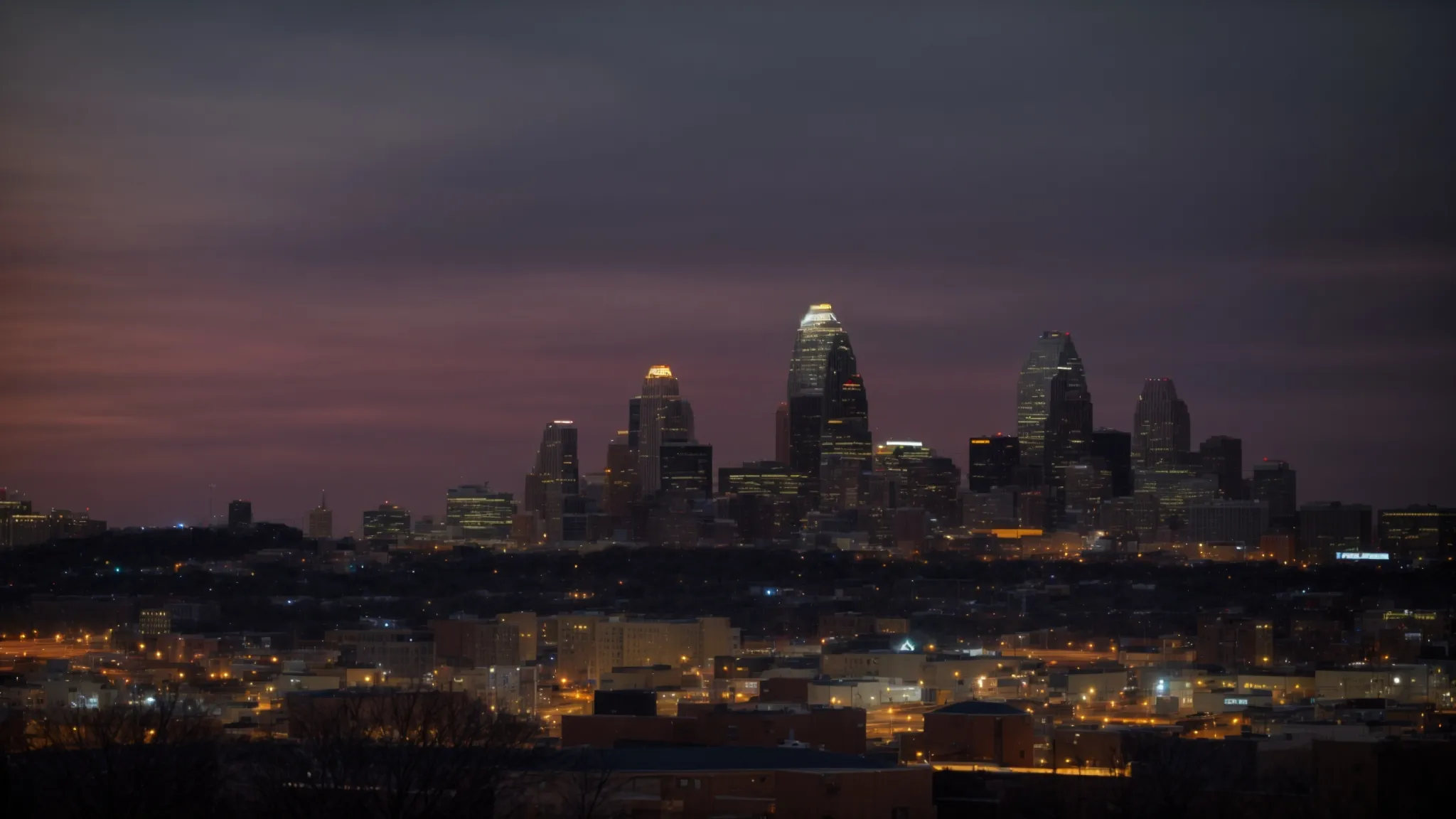 a skyline view of kansas city at dusk, showcasing the lit-up outlines of buildings against a backdrop of fading sunlight.