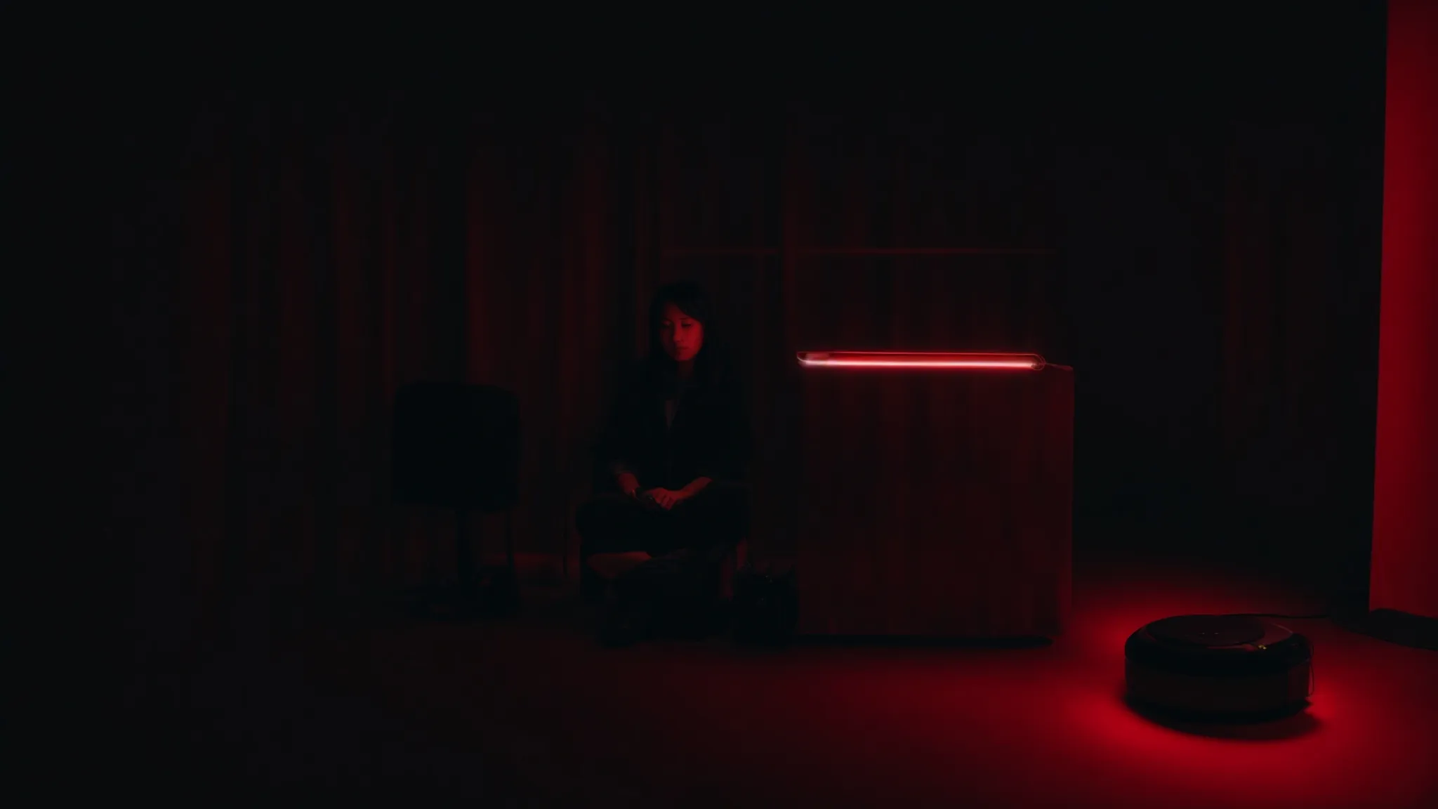 a person sits comfortably in a dimly lit room while a soft red glow emanates from a therapy device positioned in front of their face.