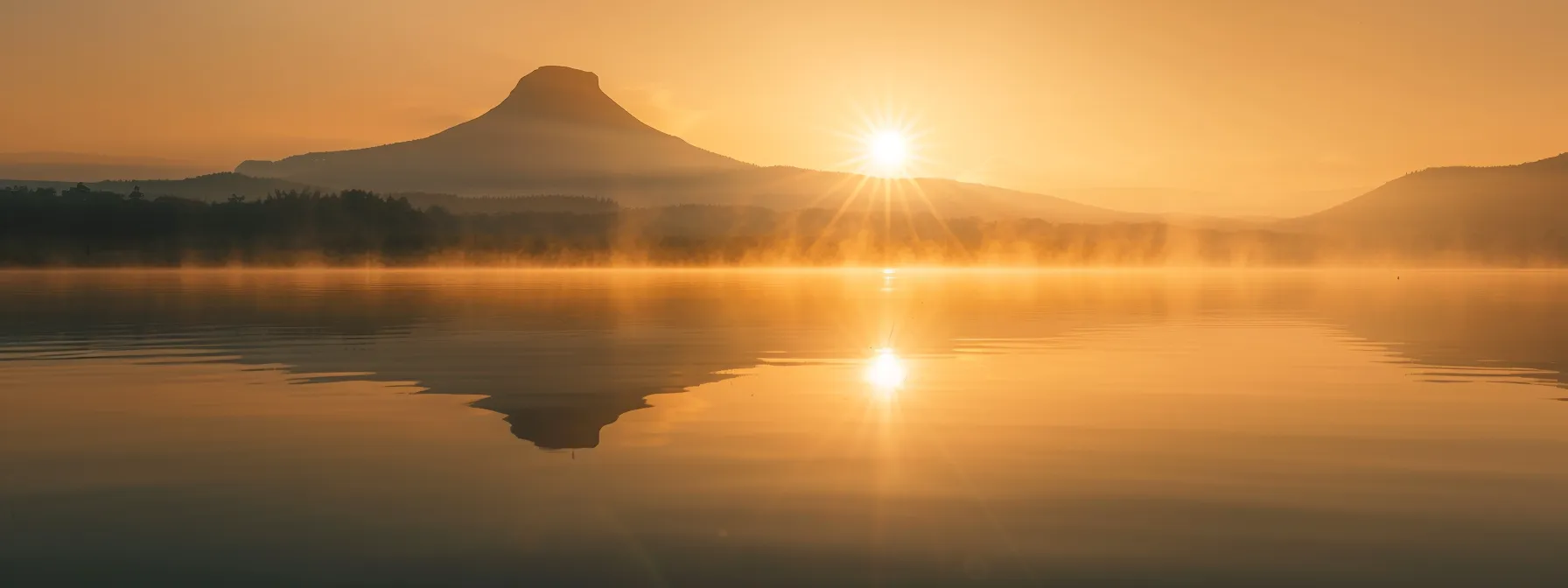 a vibrant sunrise casts golden rays over a tranquil lake, reflecting the majestic silhouette of a lone mountain, enveloped in ethereal mist.