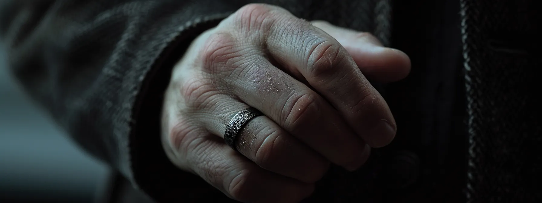 a close-up shot of a masculine hand wearing a shiny silver ring.