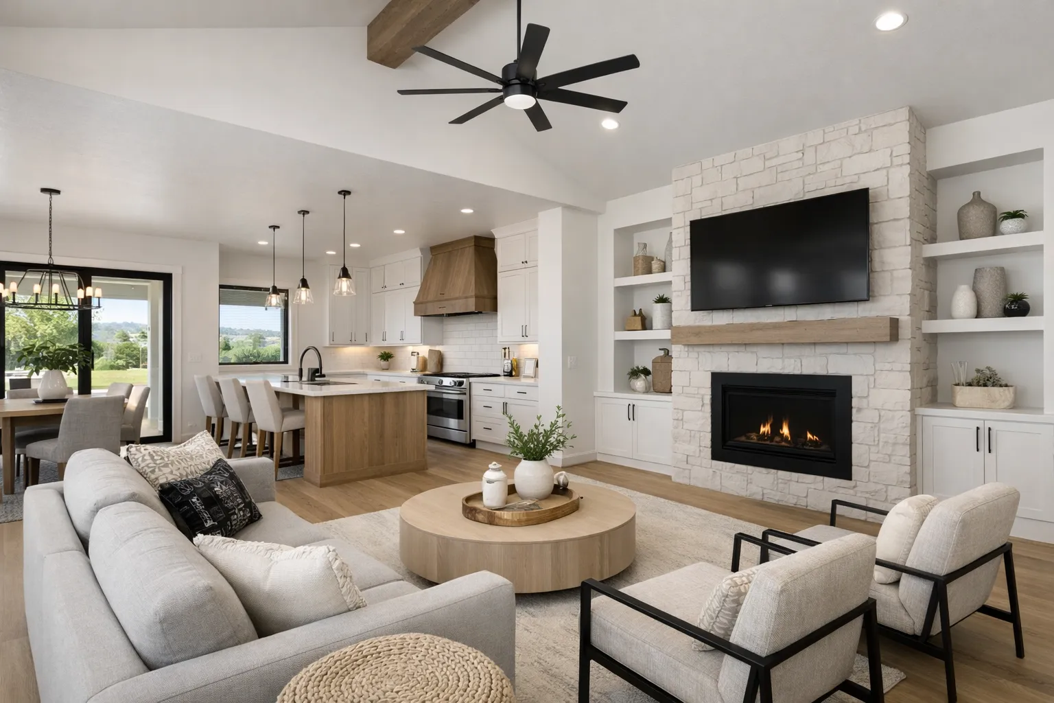 Modern professionally staged open-concept living room and kitchen in a new construction Boise or Eagle Idaho home featuring light neutral furnishings, white cabinetry, stone fireplace, wood accents, large windows, and bright natural light. Modern professionally staged open-concept living room and kitchen in a new construction Boise or Eagle Idaho home featuring light neutral furnishings, white cabinetry, stone fireplace, wood accents, large windows, and bright natural light.