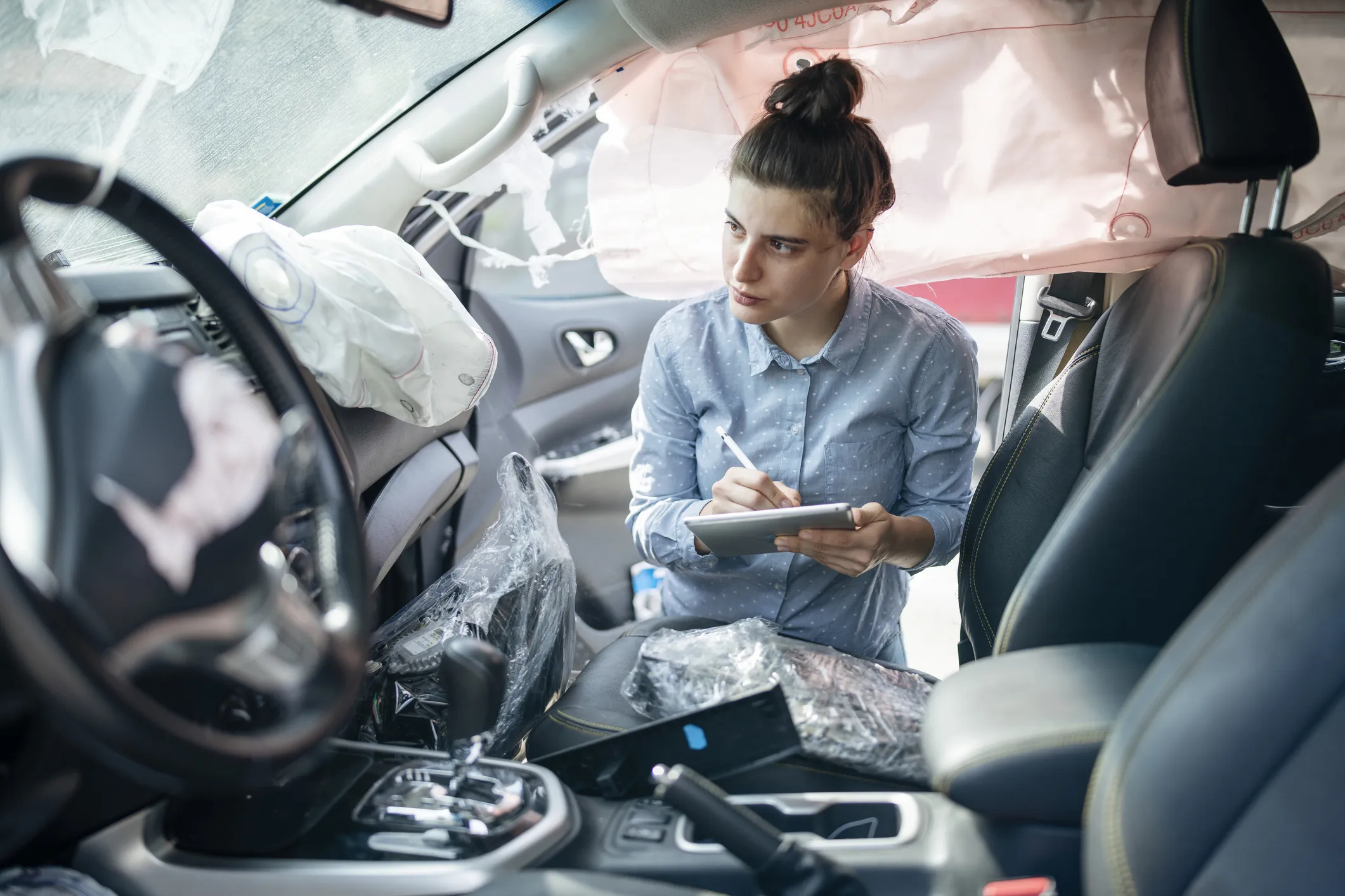 Female Insurence adjuster using digital tablet to inspect damages on the inside of a crashed vehicle.