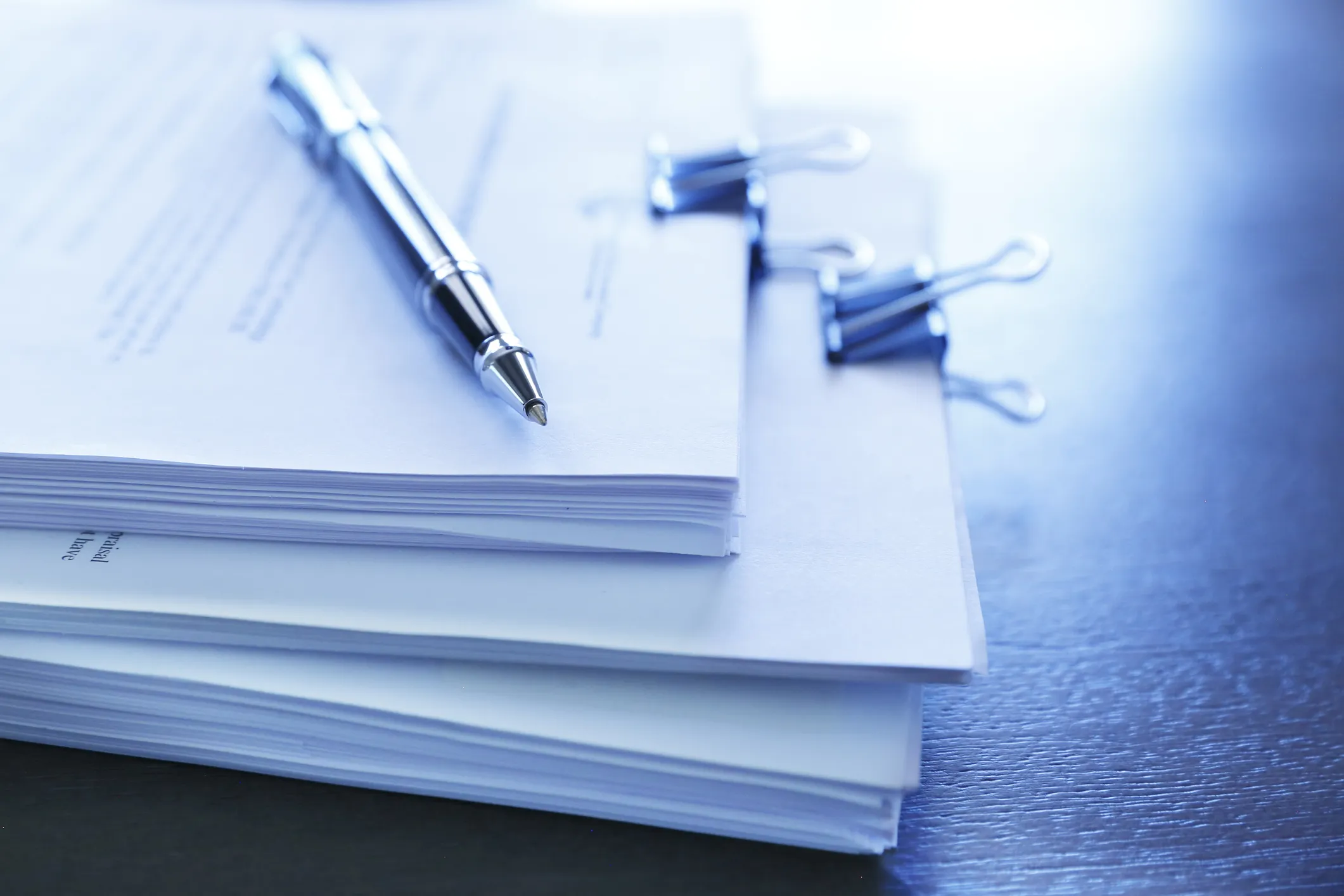 A ballpoint pen rests on top of a stack of legal documents ready for signing in Bromley. The image is photographed using a very shallow depth of field with the focus being on the tip of the pen.