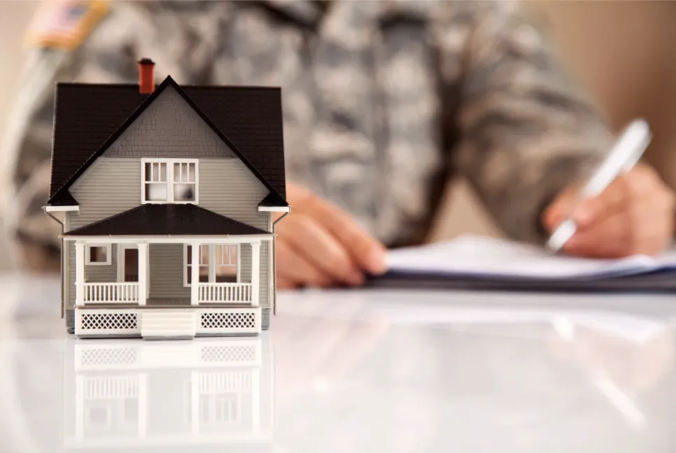 small model of a house on a desk with a blurred background of a us service member