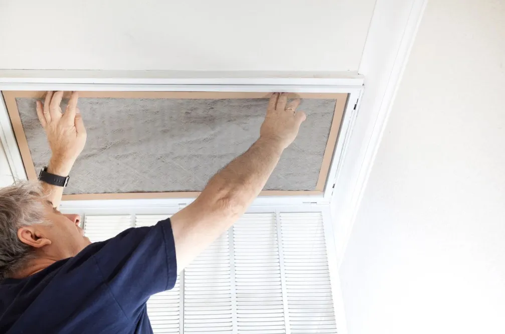Man installing or replacing a duct filter in a ceiling vent, emphasizing home maintenance and indoor air quality improvement.