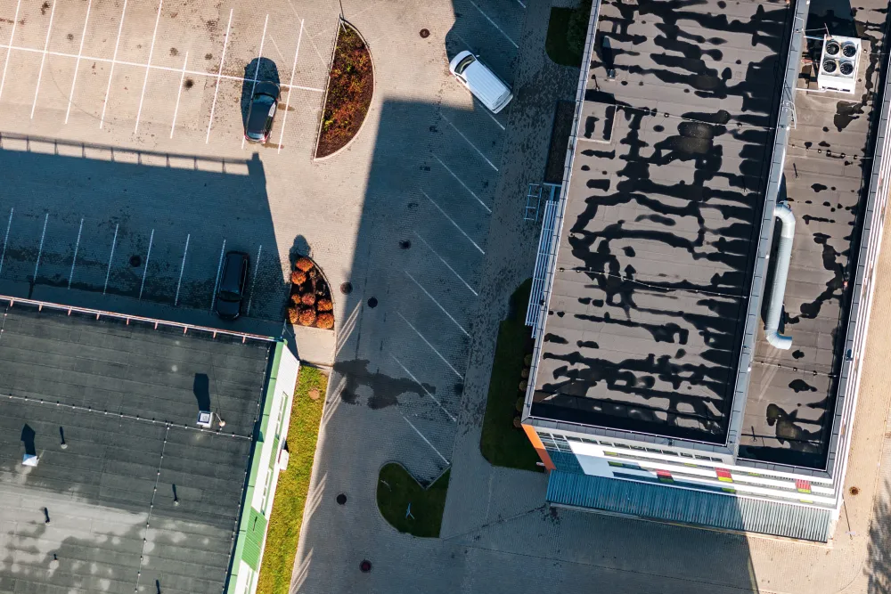 High-angle aerial view of flat commercial roofing systems on several office buildings, showing HVAC equipment and a large parking lot from above.
