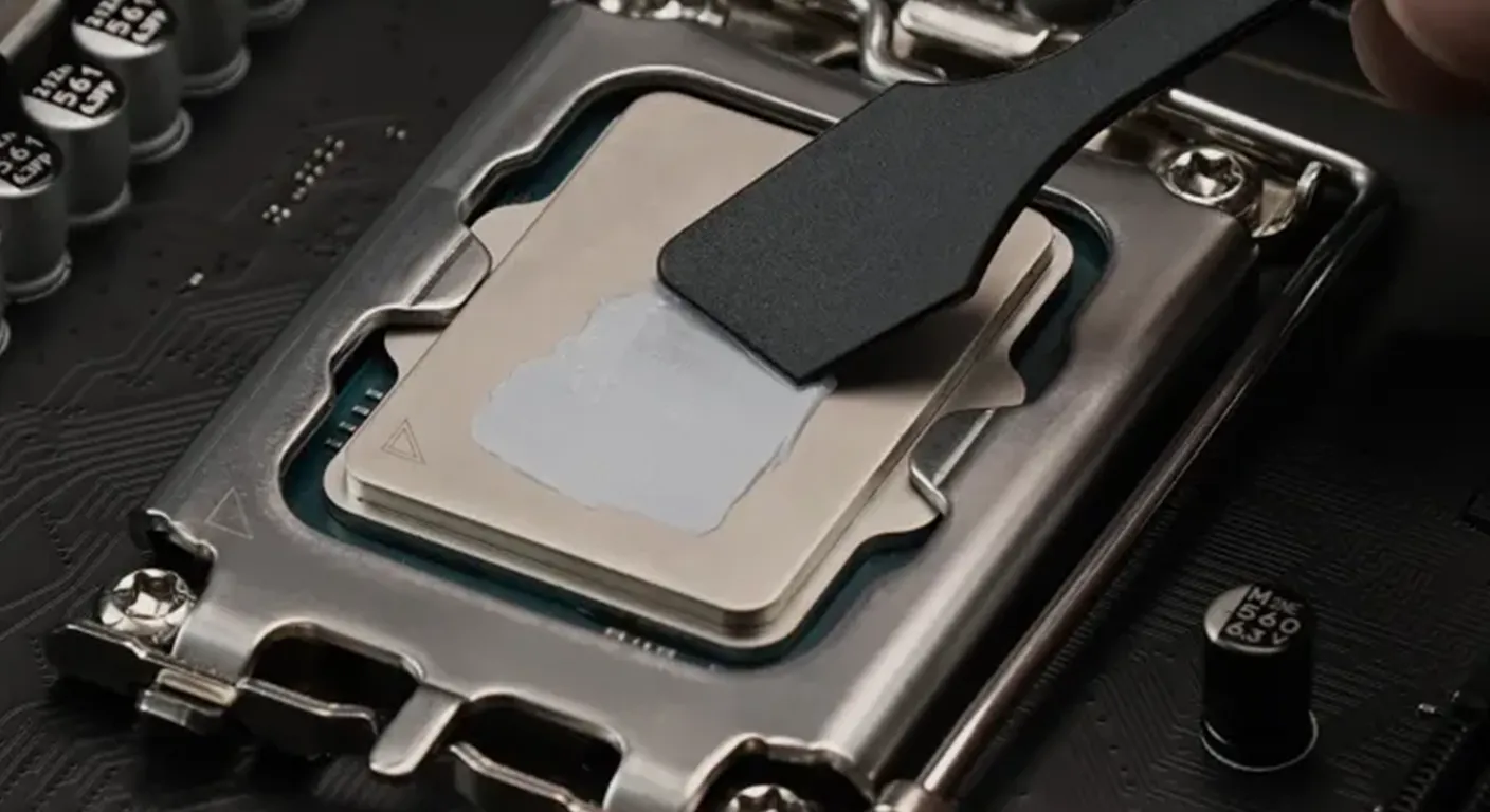 Close-up of a desktop CPU installed in a motherboard socket while thermal paste is being spread evenly across the processor surface with a plastic applicator.