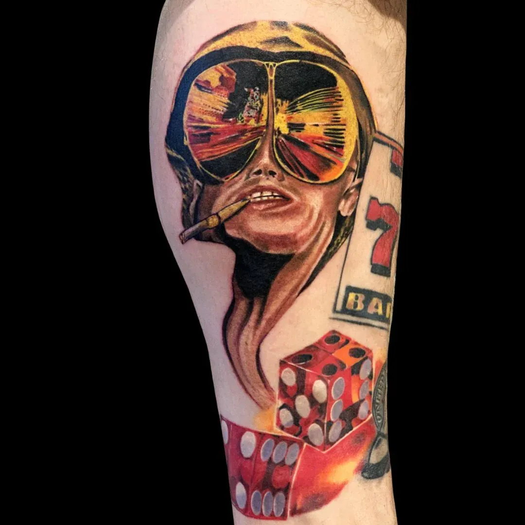 A vibrant, realistic color tattoo on a leg featuring a character in aviator sunglasses reflecting a desert scene, accompanied by red dice and a "Las Vegas" sign.