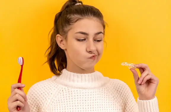 A patient at Issa Dental holding a soft toothbrush and an Invisalign aligner, illustrating the daily hygiene routine needed to keep clear aligners clean.