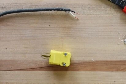Stripped electrical wire and a yellow replacement plug on a wooden workbench for a DIY repair project.