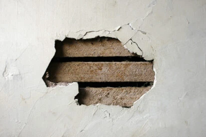 Large hole in a plaster wall exposing the wooden laths underneath, requiring home repair and patching