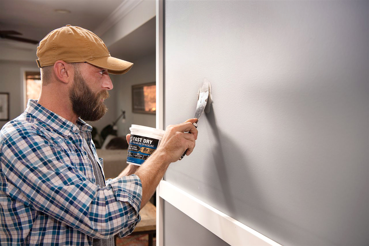 Man preparing an interior wall with a putty knife before painting