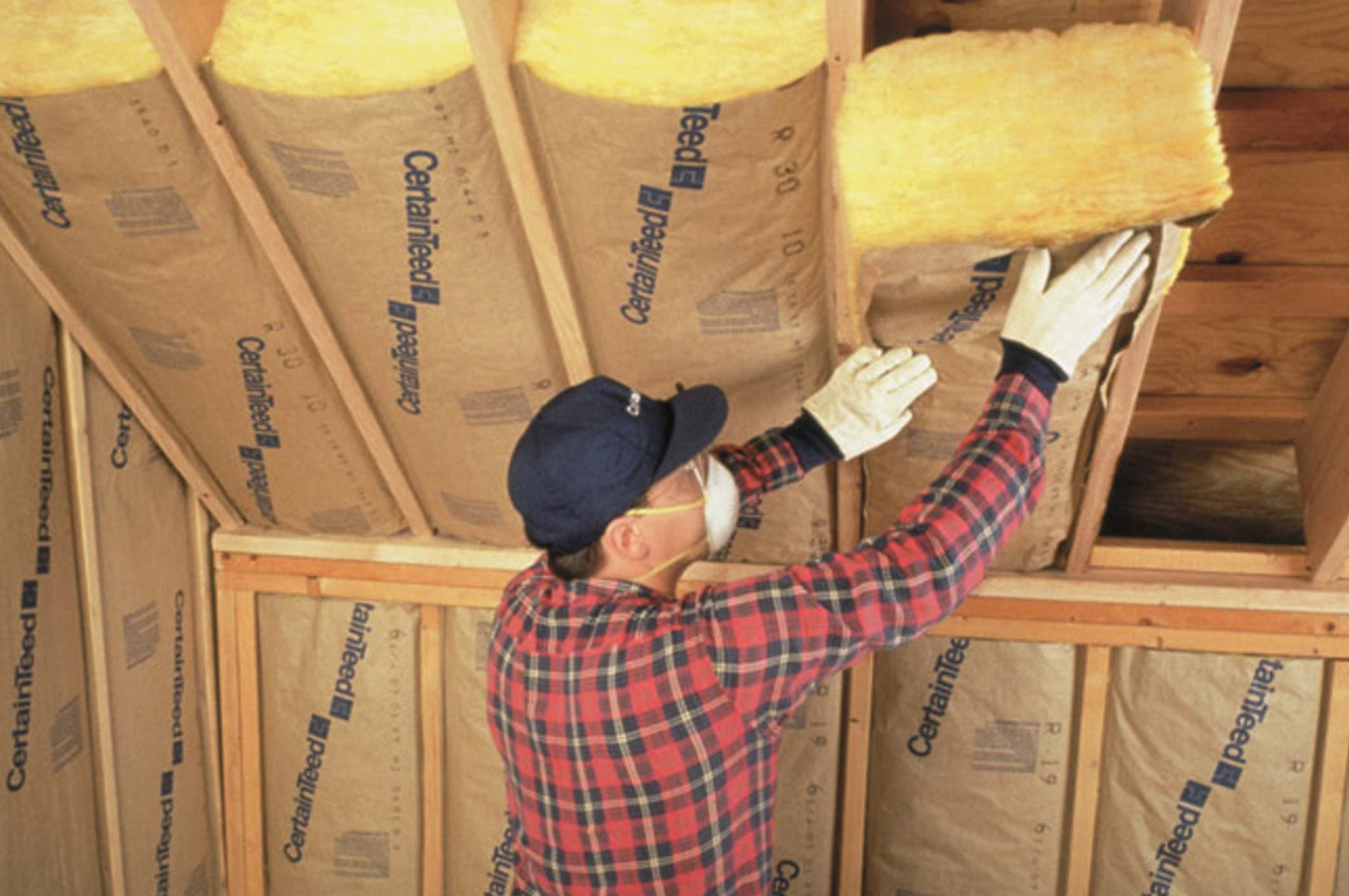 Worker installing fiberglass insulation between wooden framing